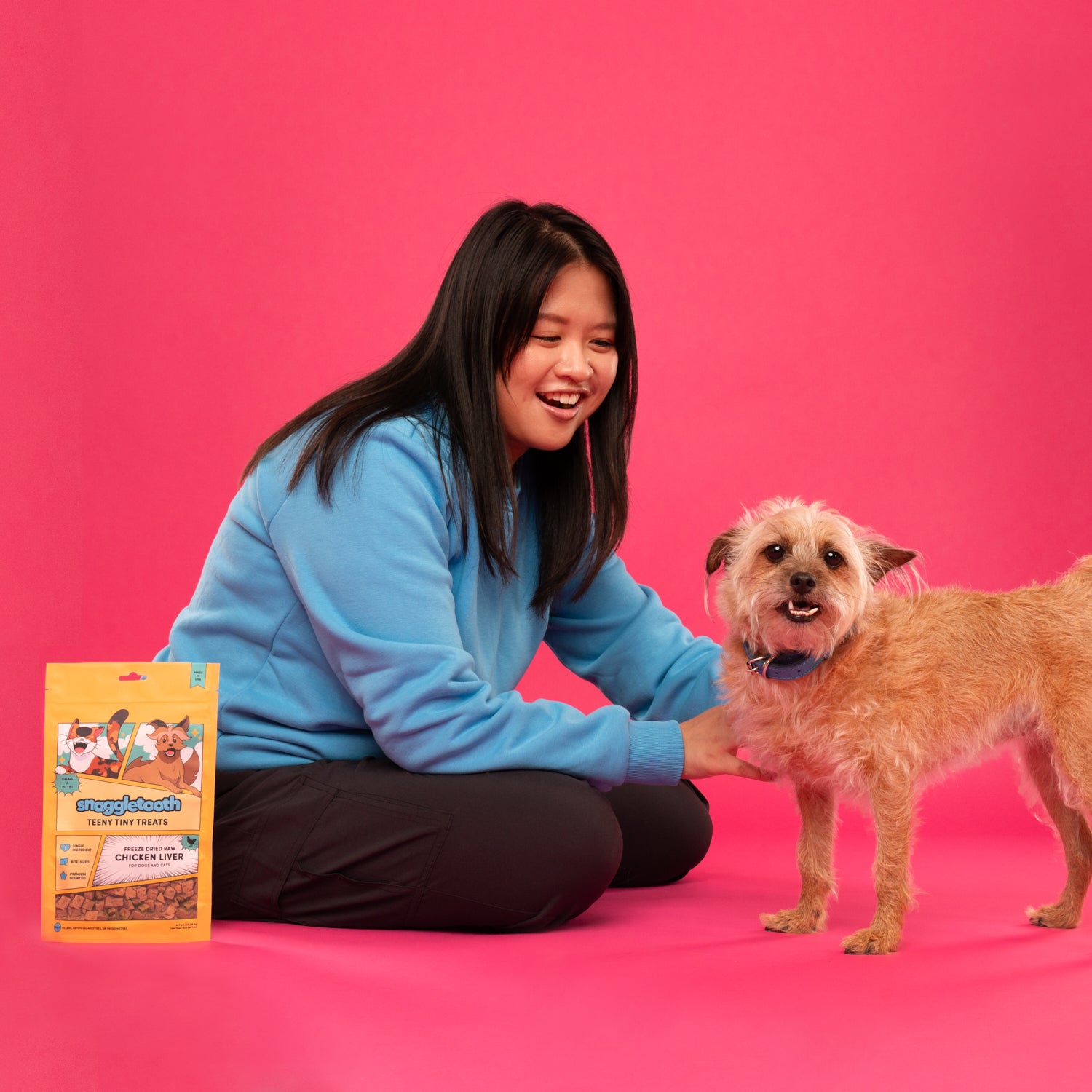 Founder Meagan petting her dog Korra next to a bag of Snaggletooth Freeze Dried Chicken Liver Treats